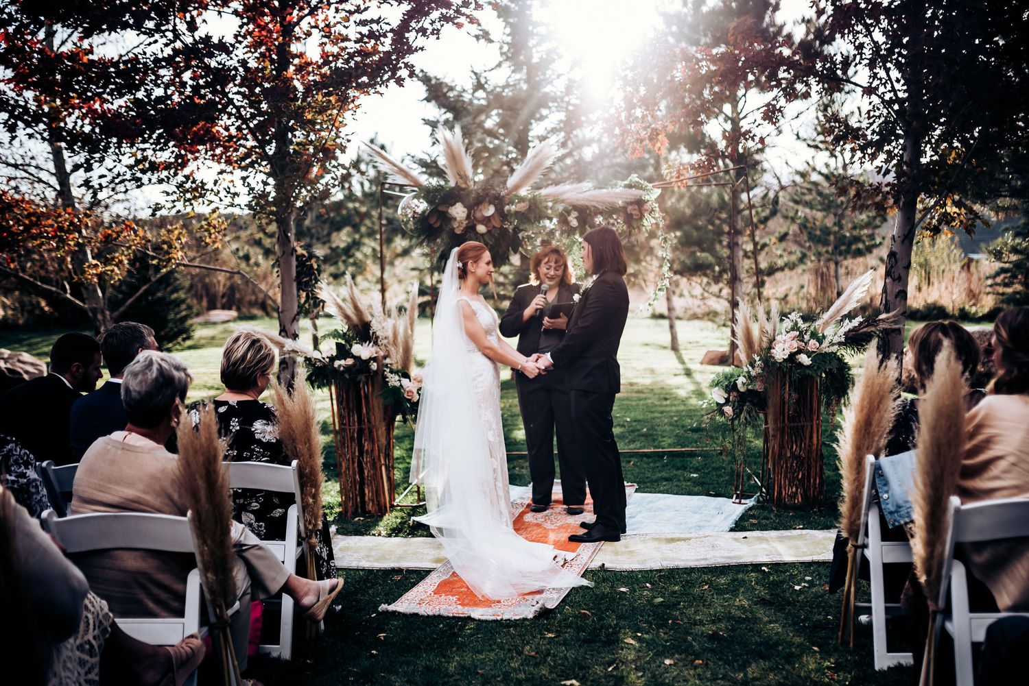 Sun-drenched outdoor wedding ceremony with white aisle runner and wooden chairs.