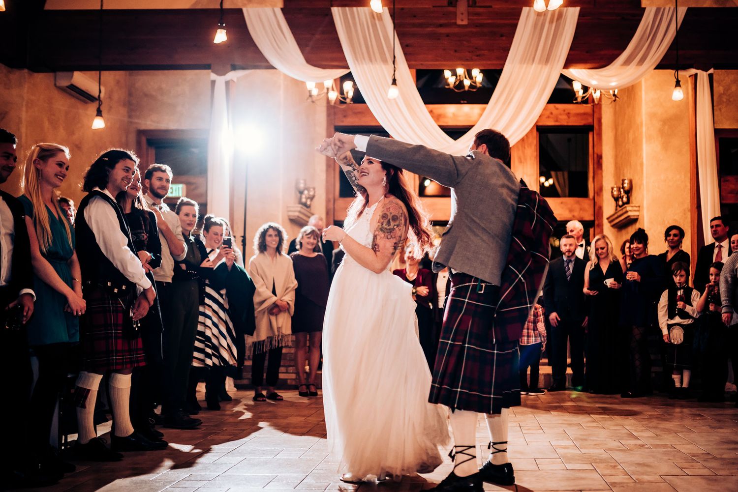 Couple performs traditional Scottish dance at wedding with guests watching.