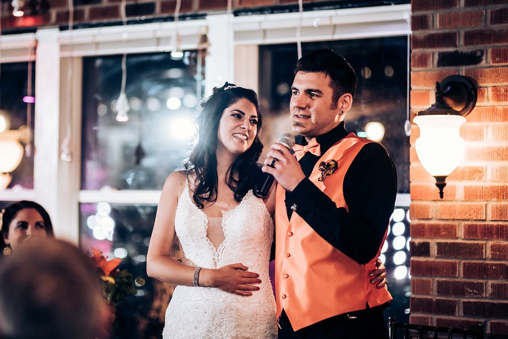 Wedding reception couple making a speech together at an indoor venue with brick walls and mood lighting.