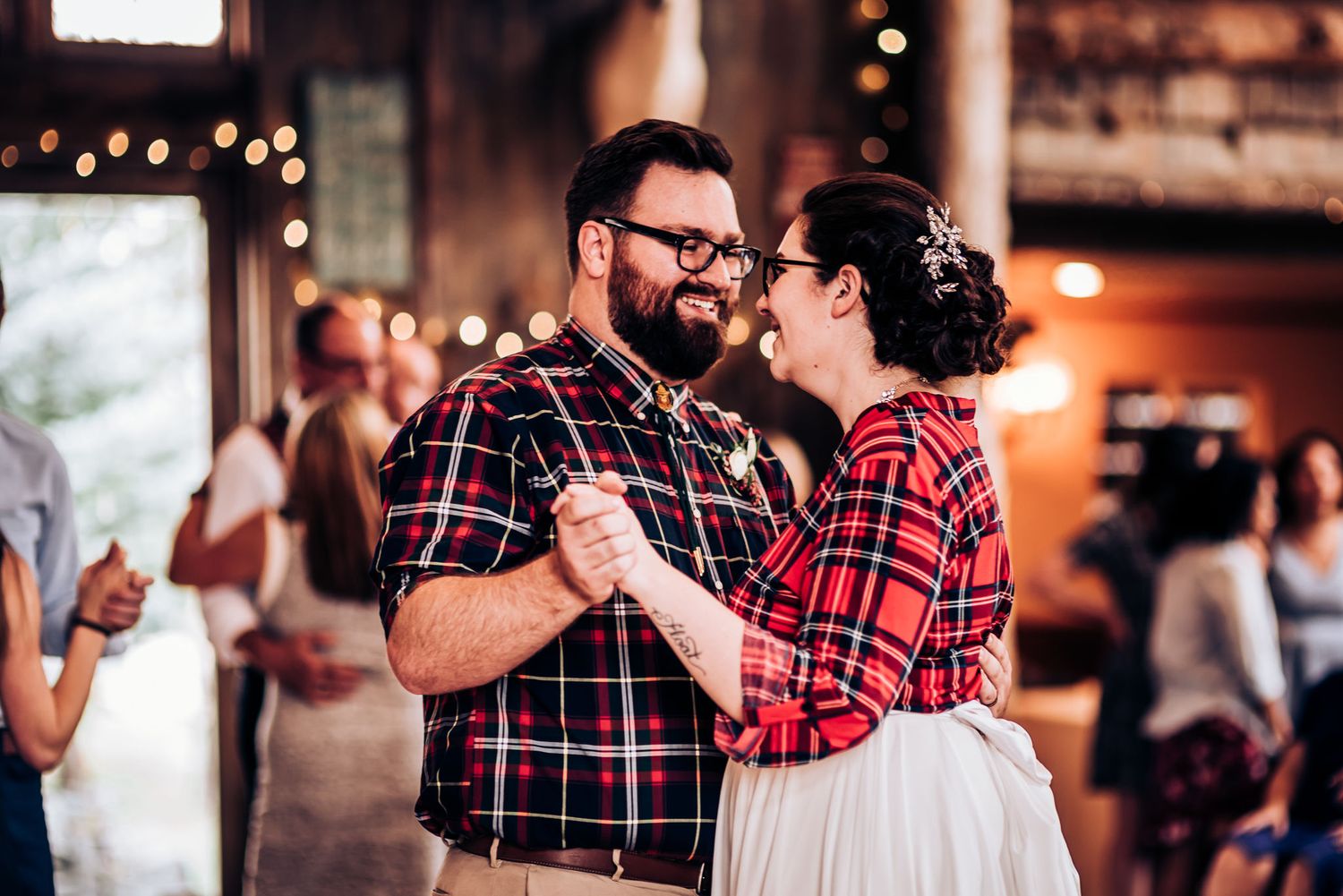 Matching couple in red plaid shirts dancing together at indoor reception venue.