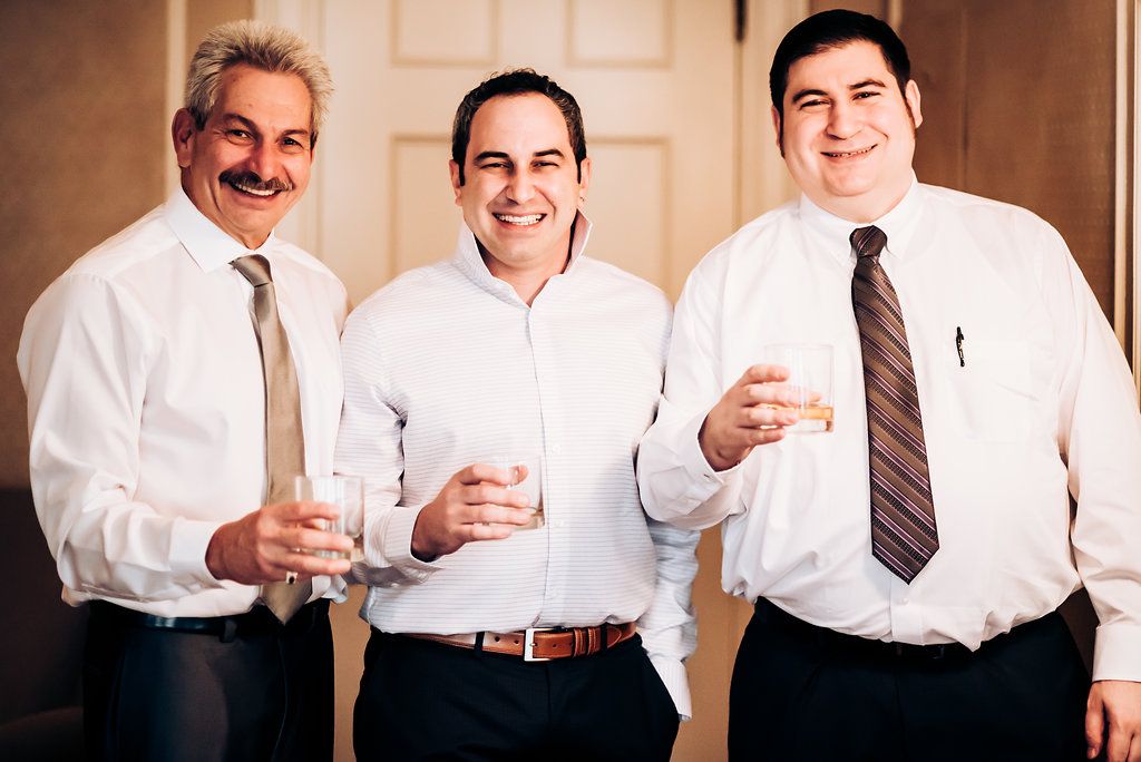 Three men in white dress shirts and ties share drinks together at a formal event.