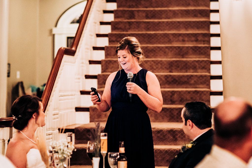 Speaker gives heartfelt toast during wedding reception by elegant staircase.