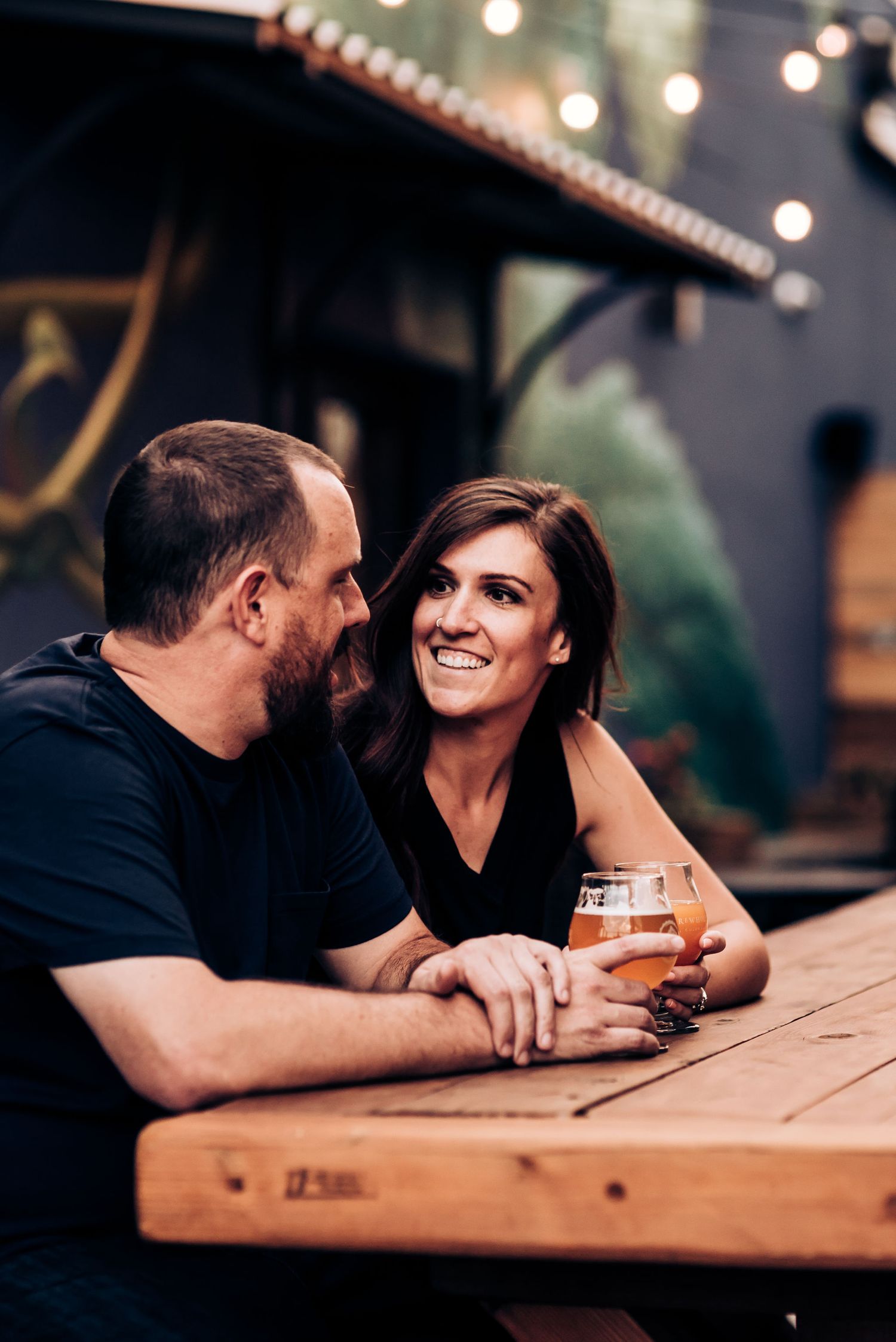 Couple enjoying drinks and conversation at outdoor wooden table.