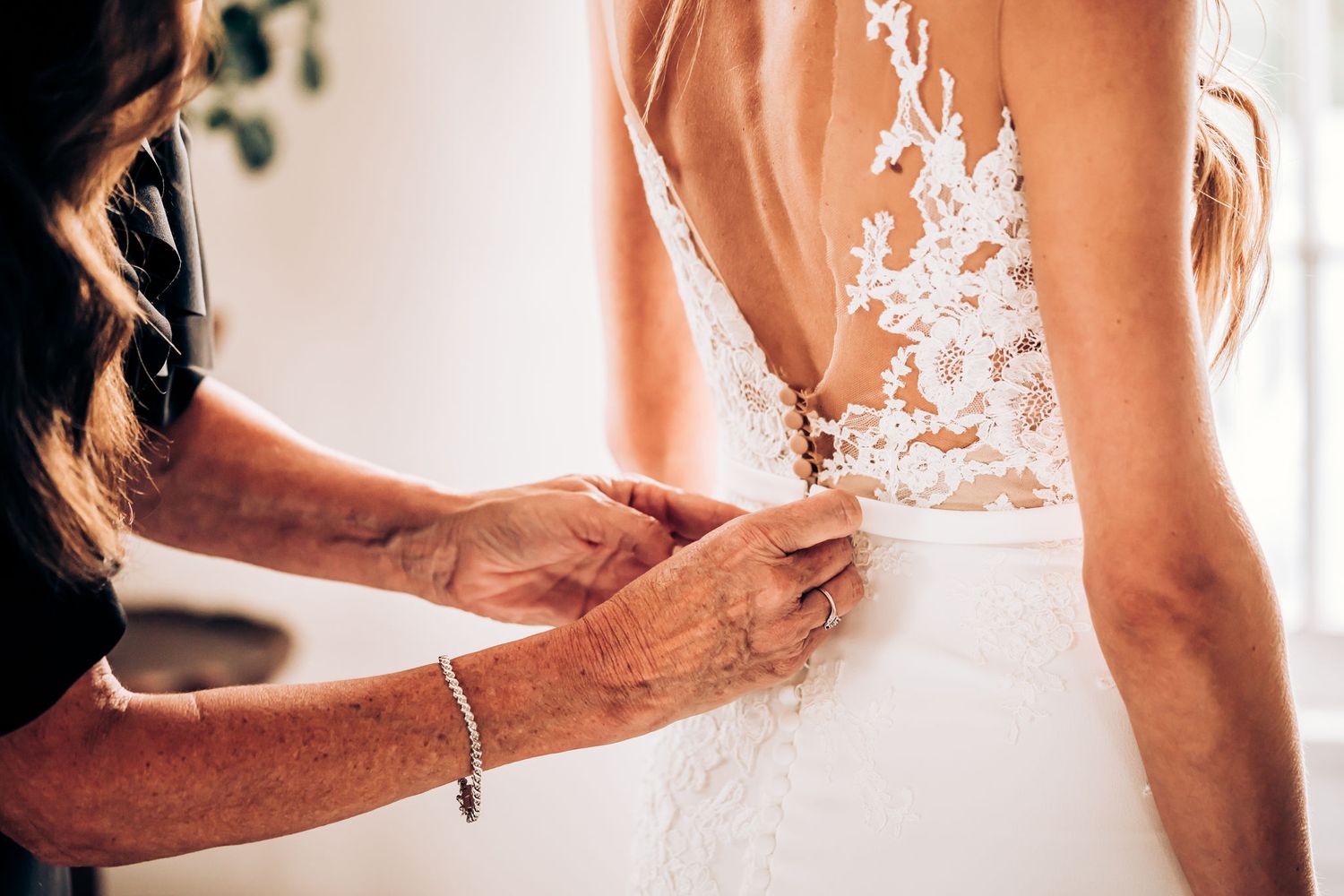 Close-up of delicate lace dress buttons being fastened on wedding gown.