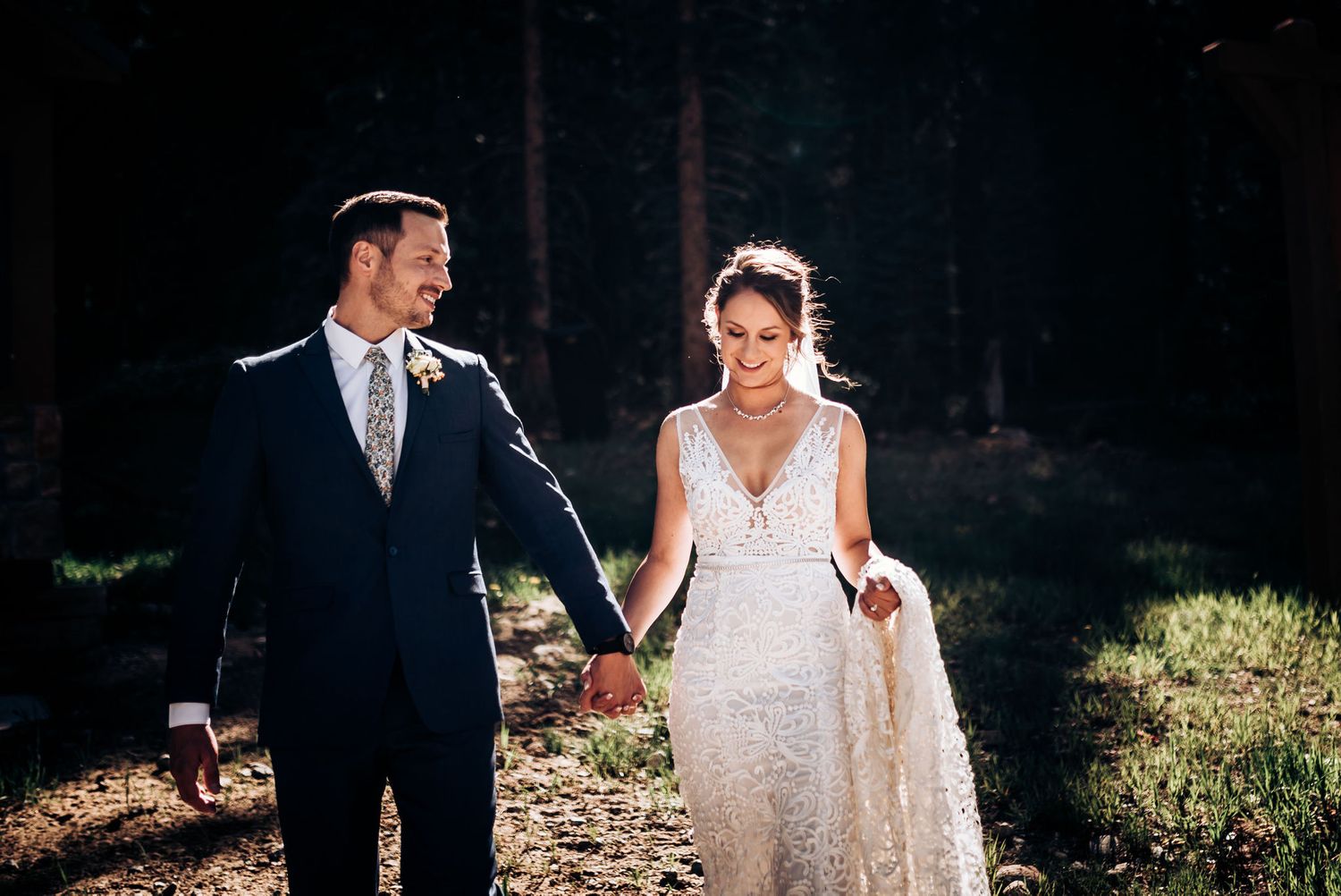 A wedding couple walking through sunlit mountain terrain during their ceremony.