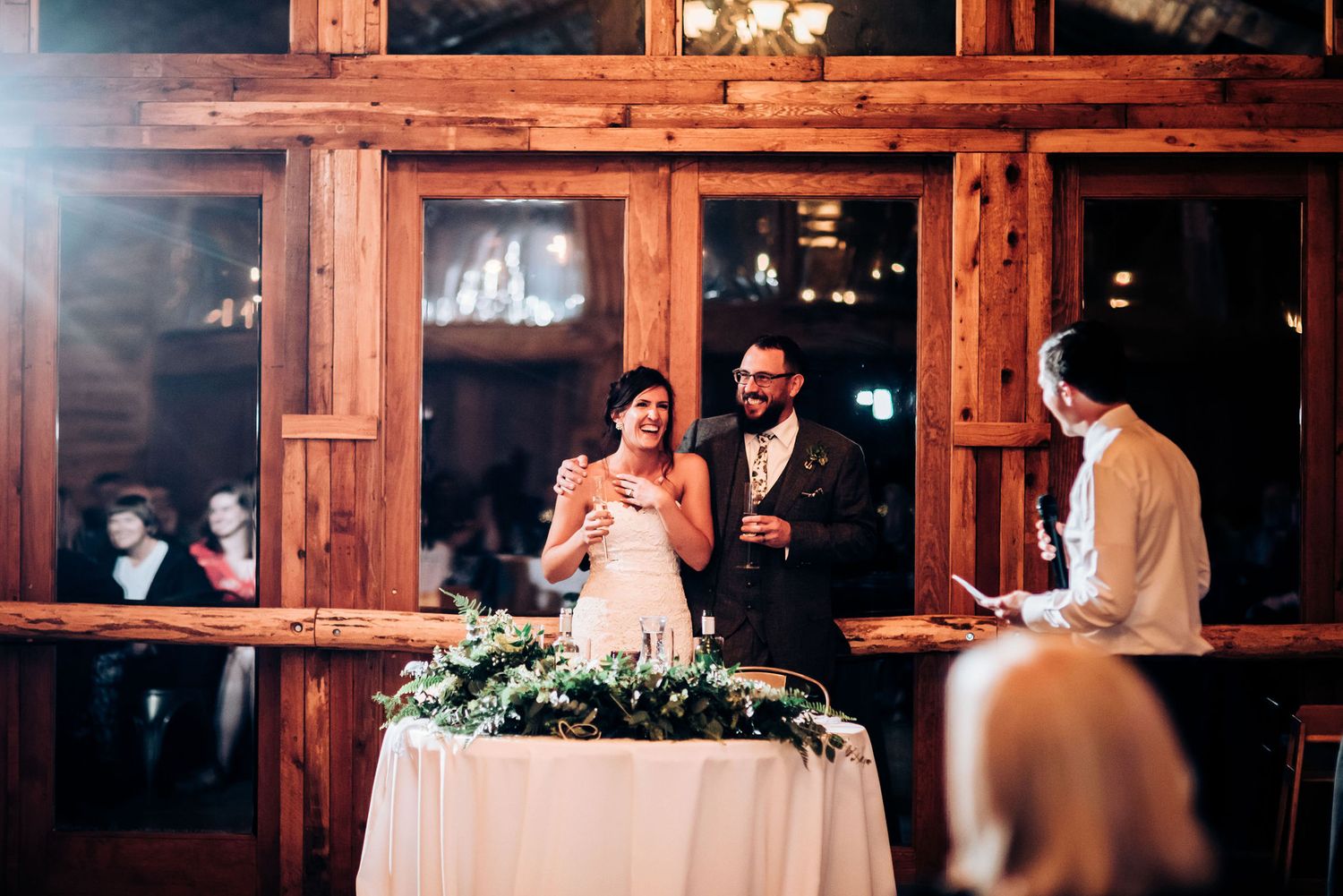 Wedding reception speech moment in rustic venue with floral table decorations.