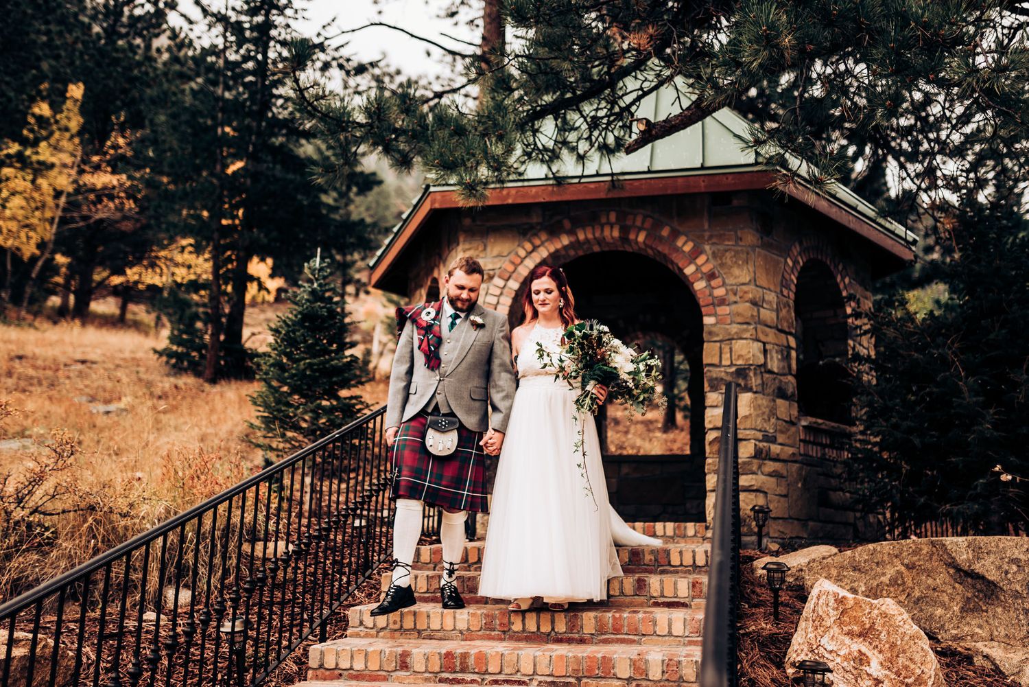 A couple poses in a rustic stone archway during their mountain wedding ceremony.
