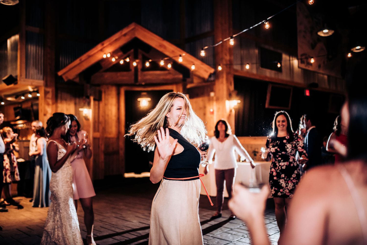Wedding guests dance and celebrate on rustic wooden dance floor with cabin-style architecture.