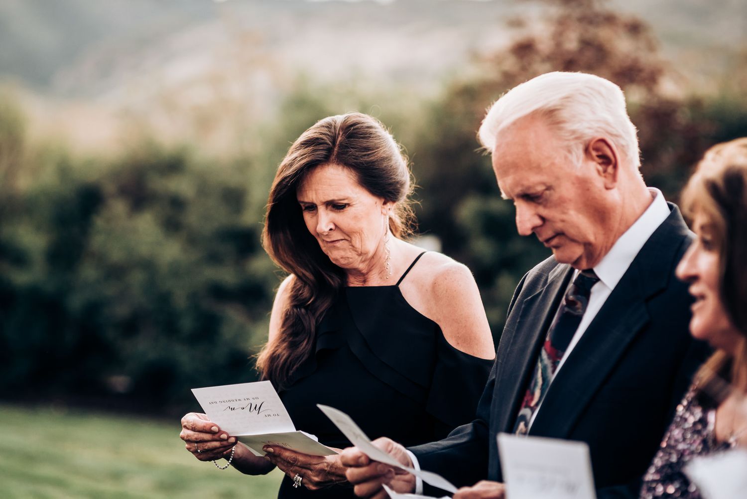 A group reads from papers during an outdoor ceremony at sunset.