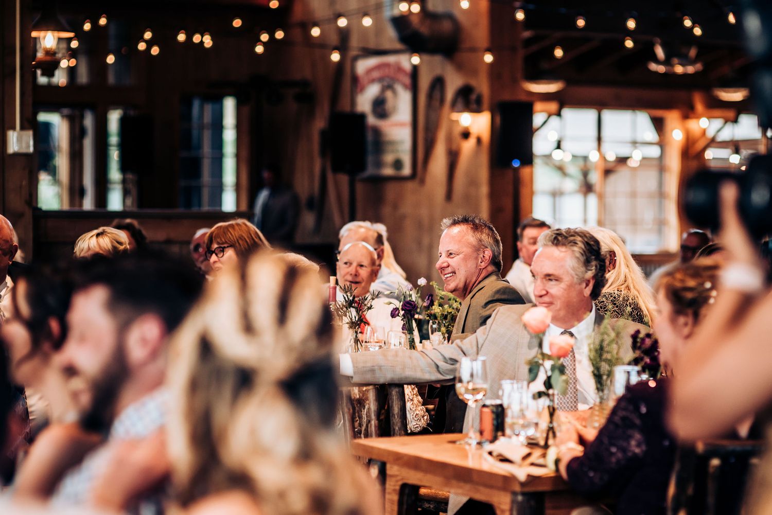 Wedding guests cheering and celebrating at rustic venue with string lights overhead.