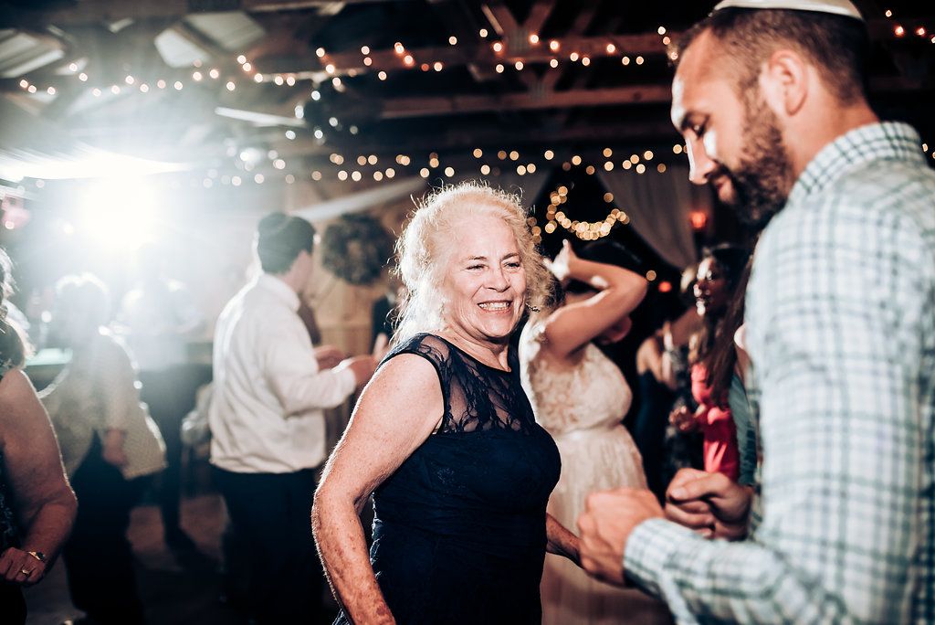 Wedding guests dance and laugh together under twinkling lights at an evening reception.