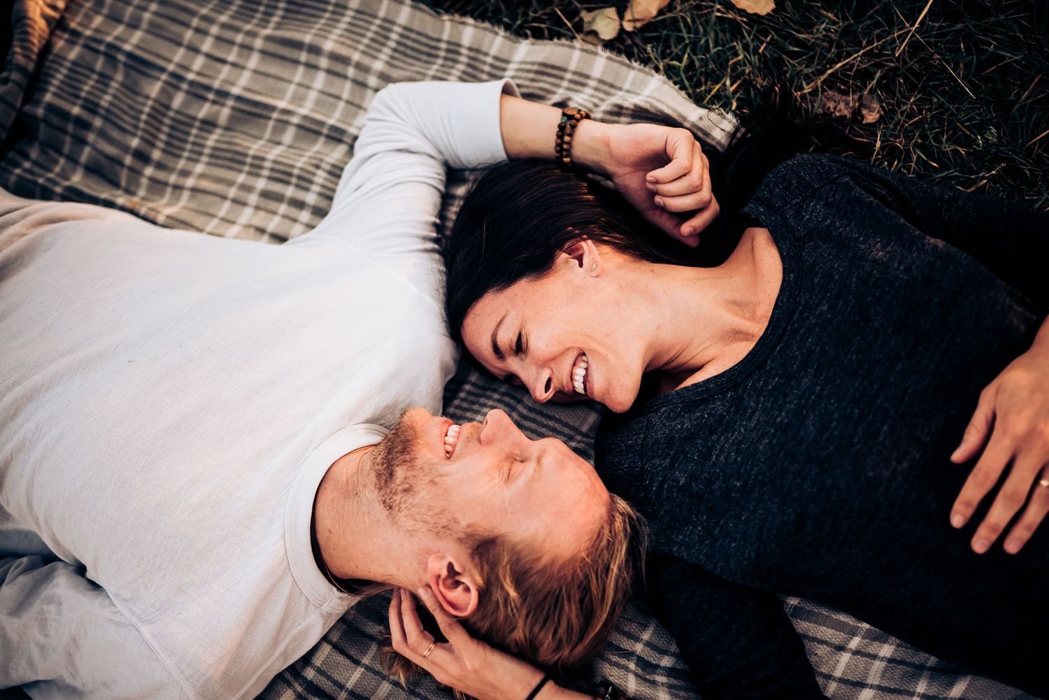 A couple lying on a plaid blanket sharing an intimate moment together outdoors.