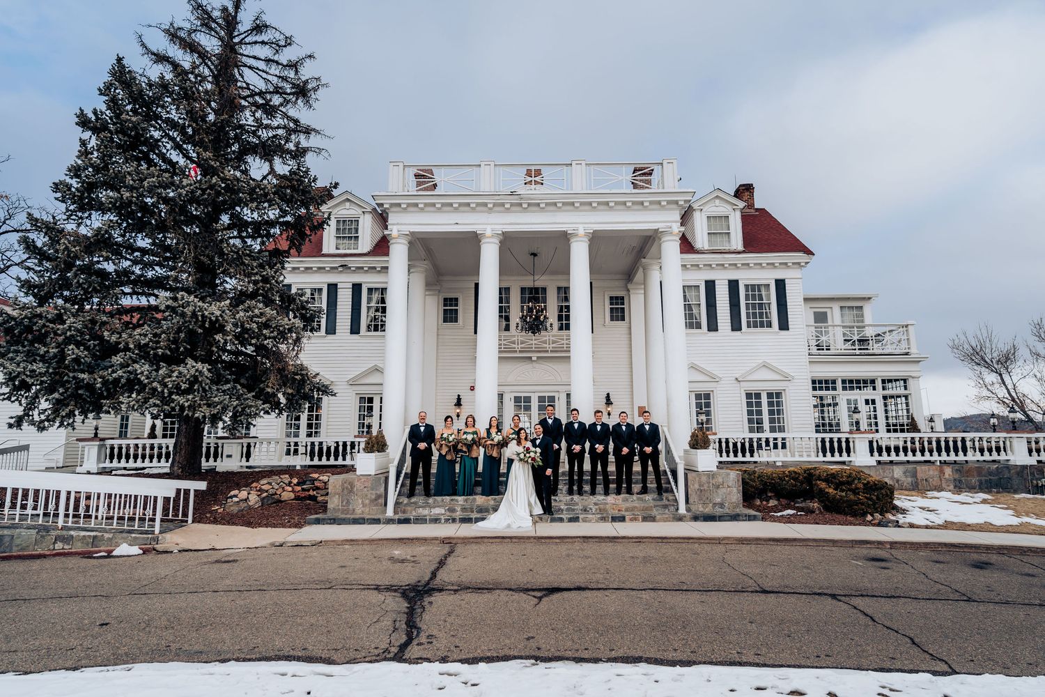 Winter wedding party photo in front of stately white colonial mansion with pillars.