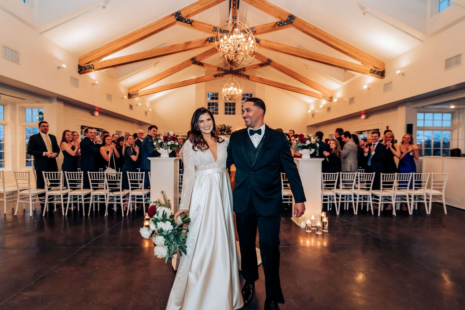 Newlyweds make their grand exit in a wedding venue with exposed wood beams and white chairs.