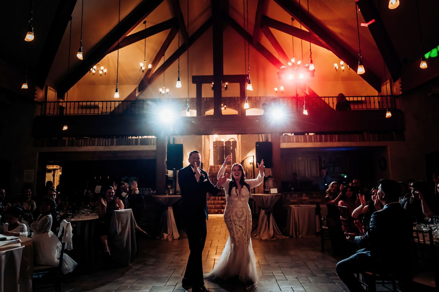 A couple dances in the spotlight under wooden beams at their wedding reception.