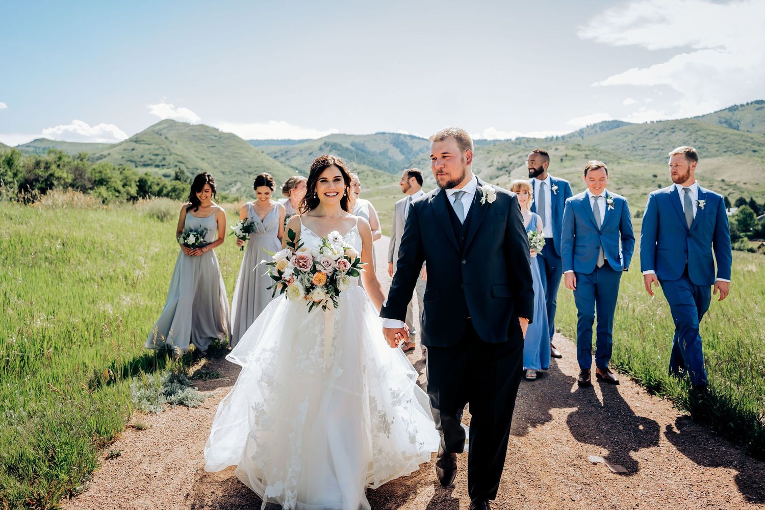 Wedding party walking together through mountain meadow with bridal party in pastel dresses.