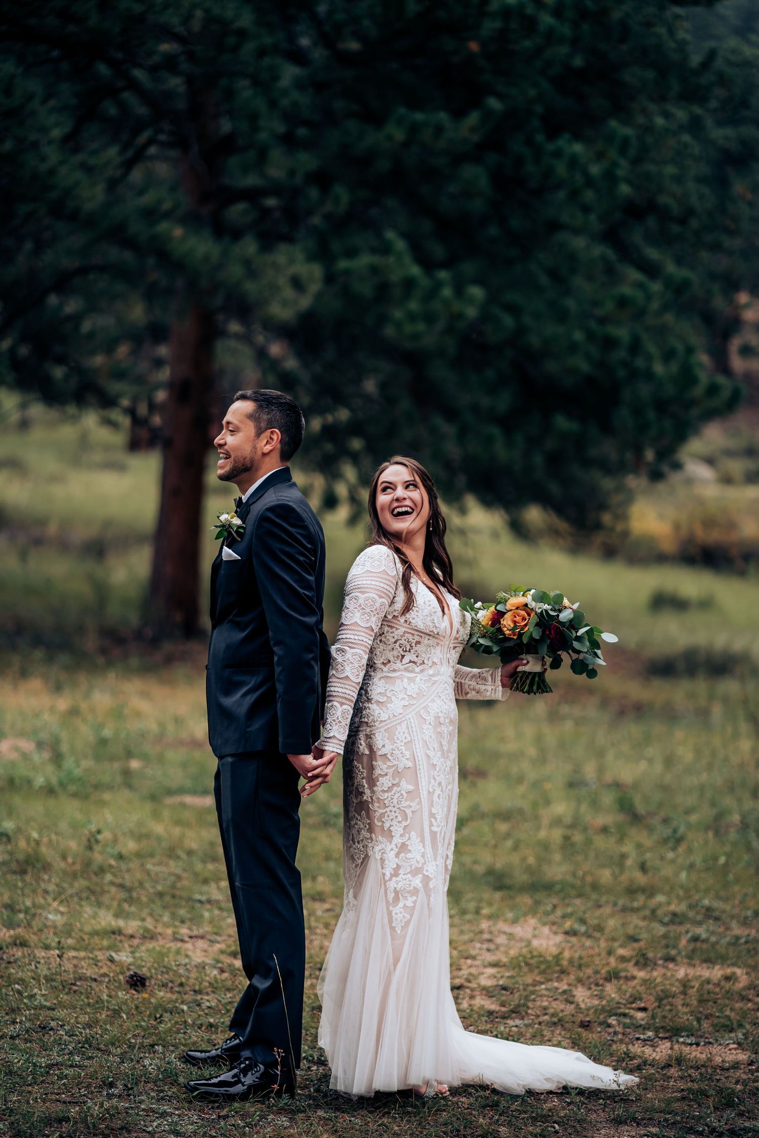 Joyful couple shares first look moment in rustic outdoor setting with pine trees.