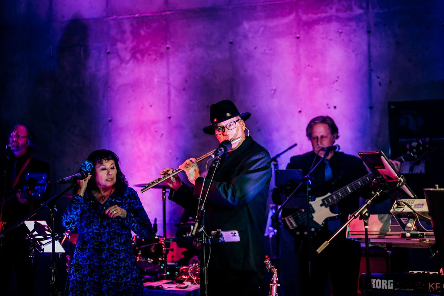 A band performs on stage with purple mood lighting and multiple musicians.