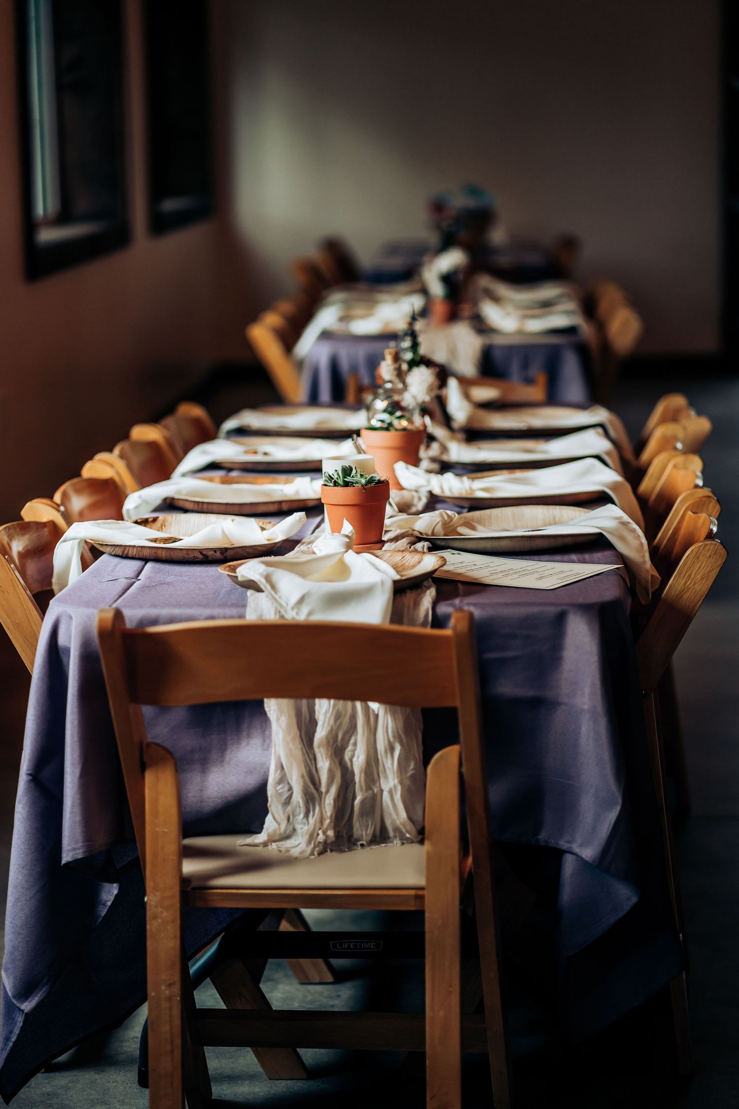 Long dining table set with purple tablecloths and wooden chairs in a rustic dining room.