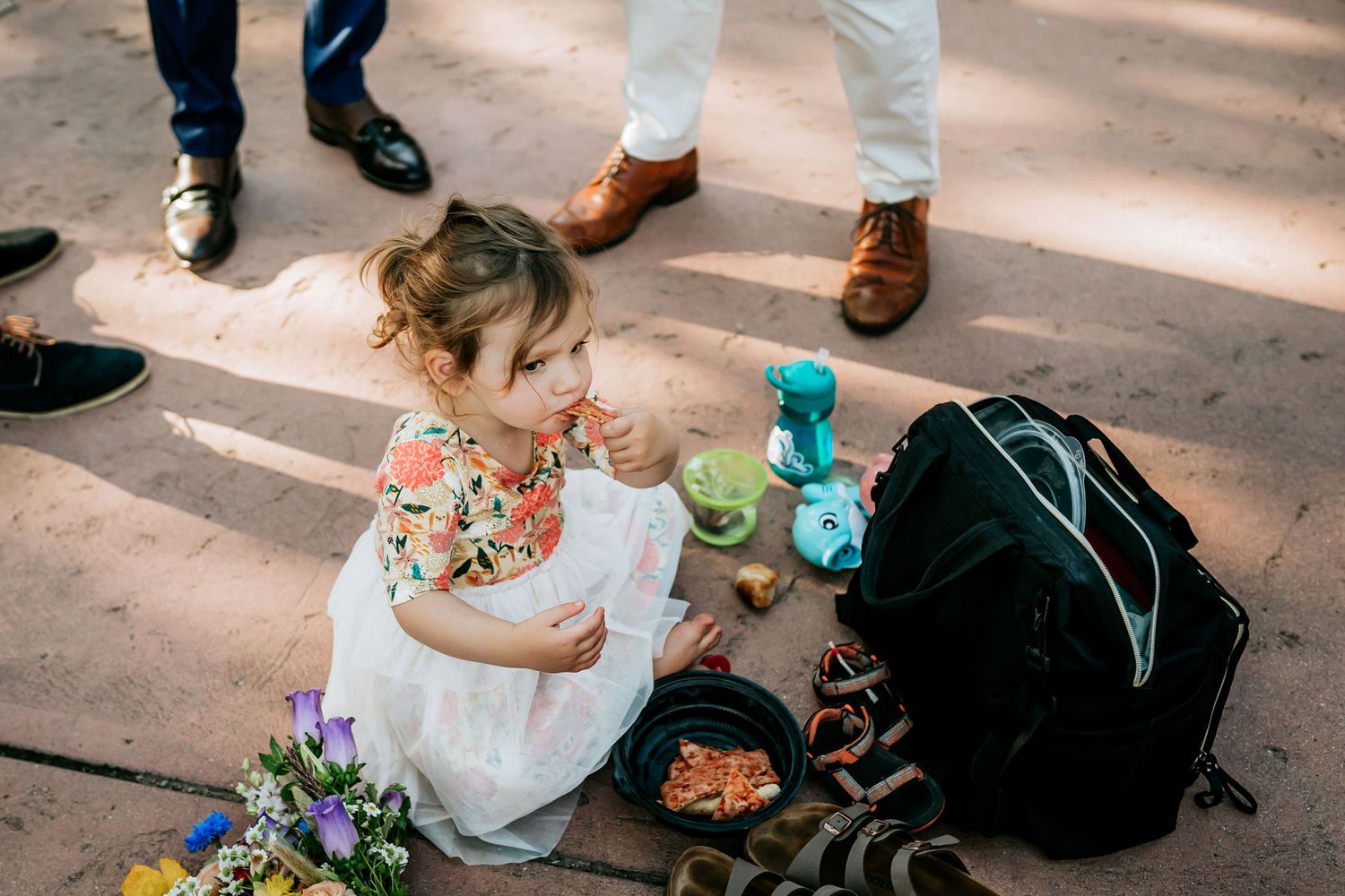A small child in a white dress plays with toys on the ground during a formal event.