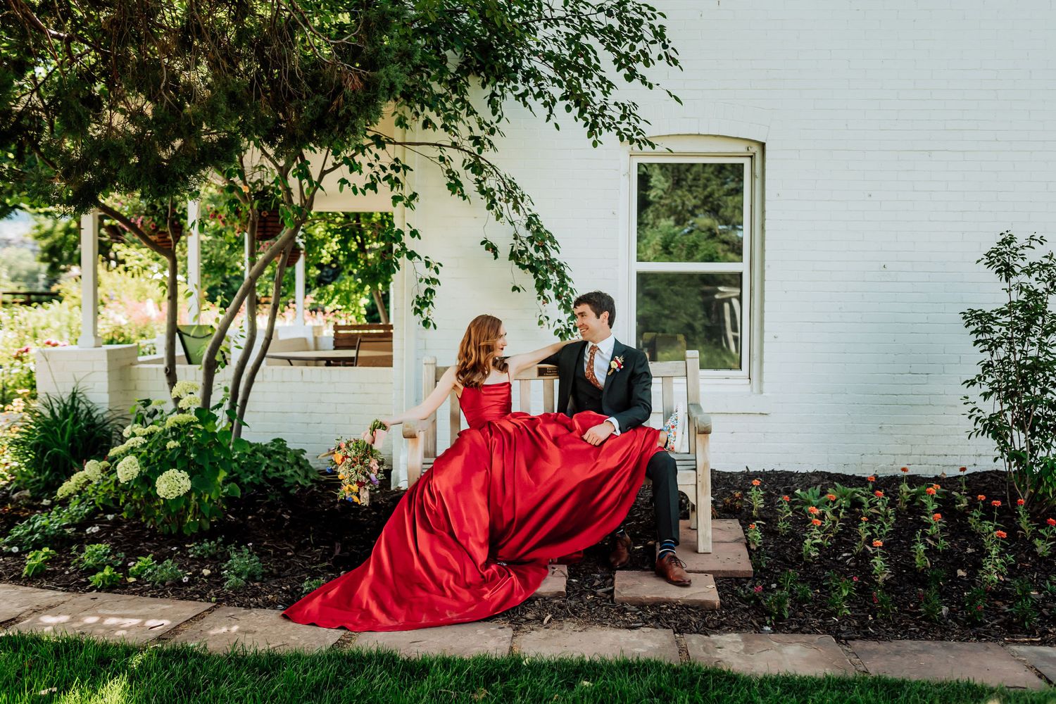 Dramatic red ballgown flowing in breeze during outdoor photo session by white building.
