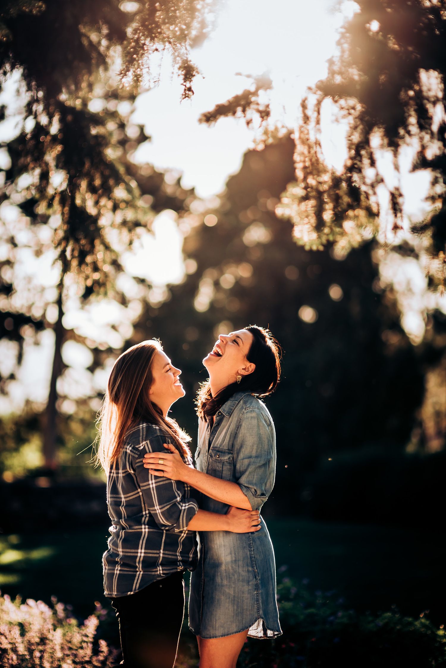 Two people share a joyful moment together in dappled sunlight under trees.