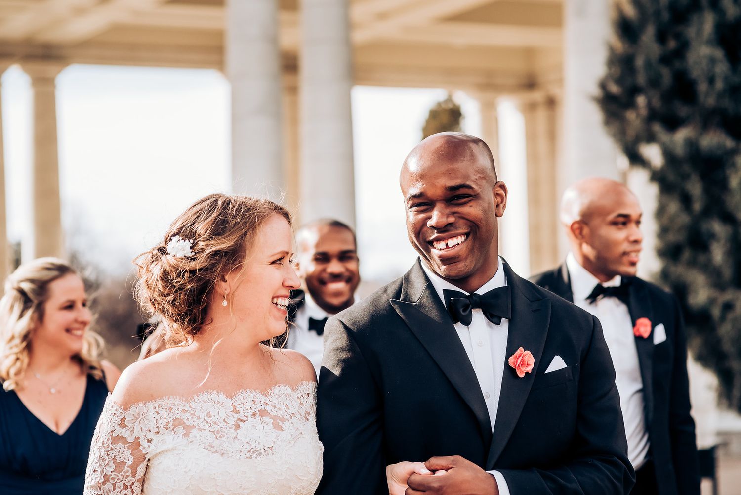 A candid moment of joy captured during an outdoor wedding celebration under white columns.