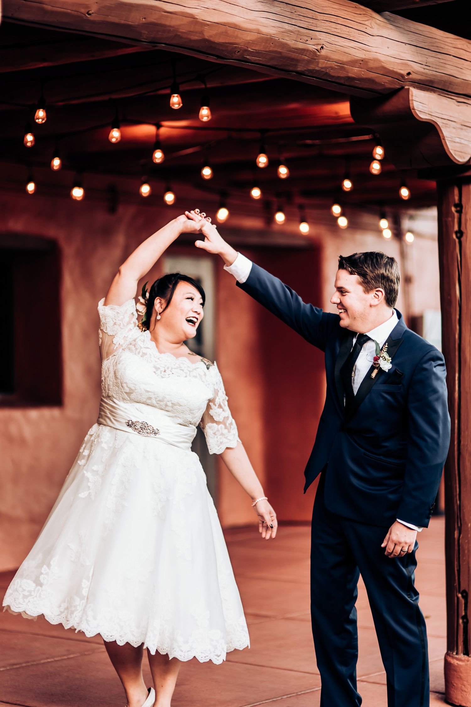 Wedding couple dancing joyfully under bistro lights on rustic terrace.