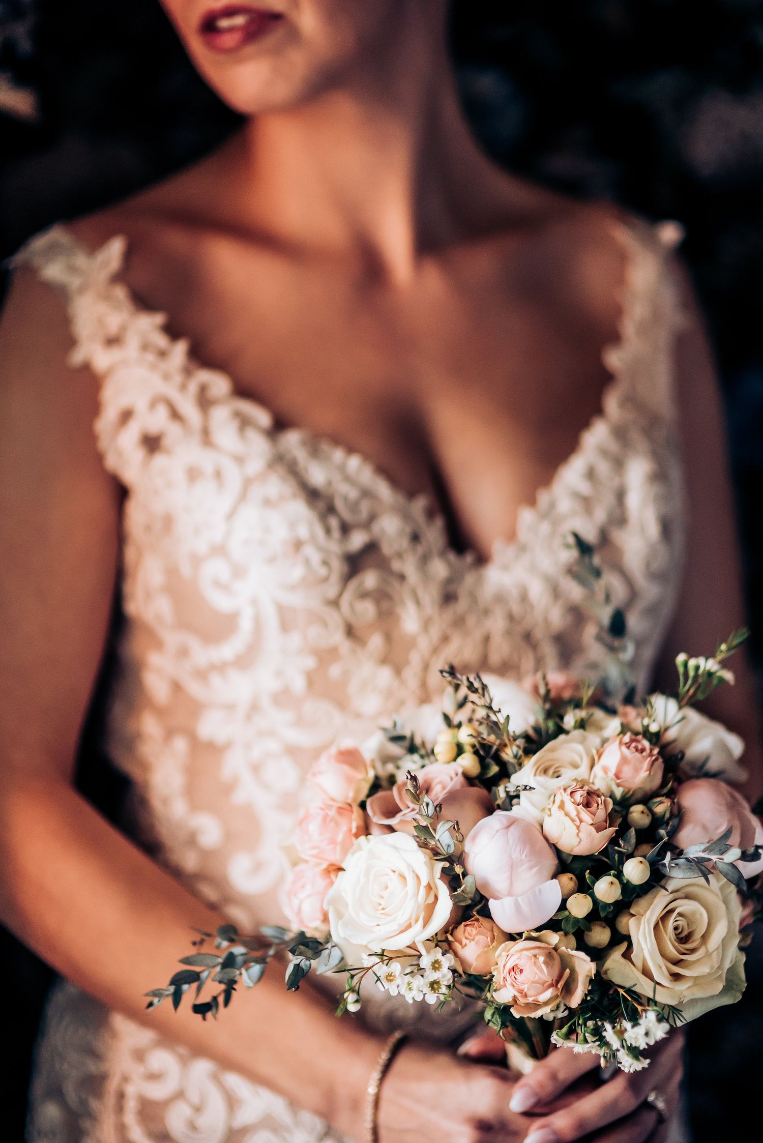 Detail shot of lace wedding dress and soft pink and white rose bouquet.