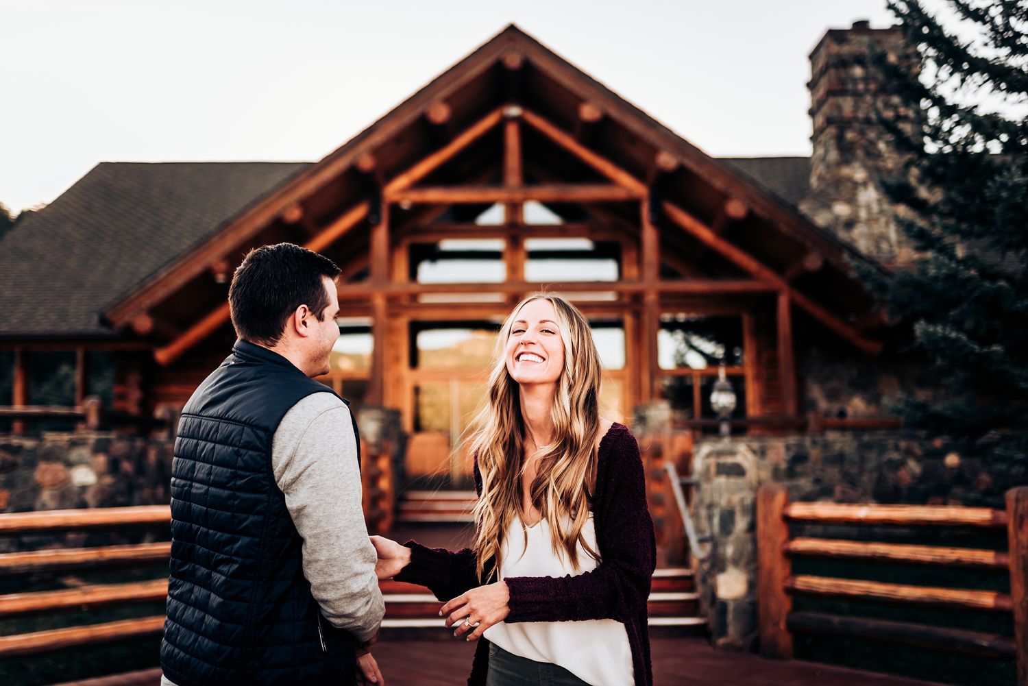 Couple sharing a joyful moment outside rustic log cabin during golden hour.