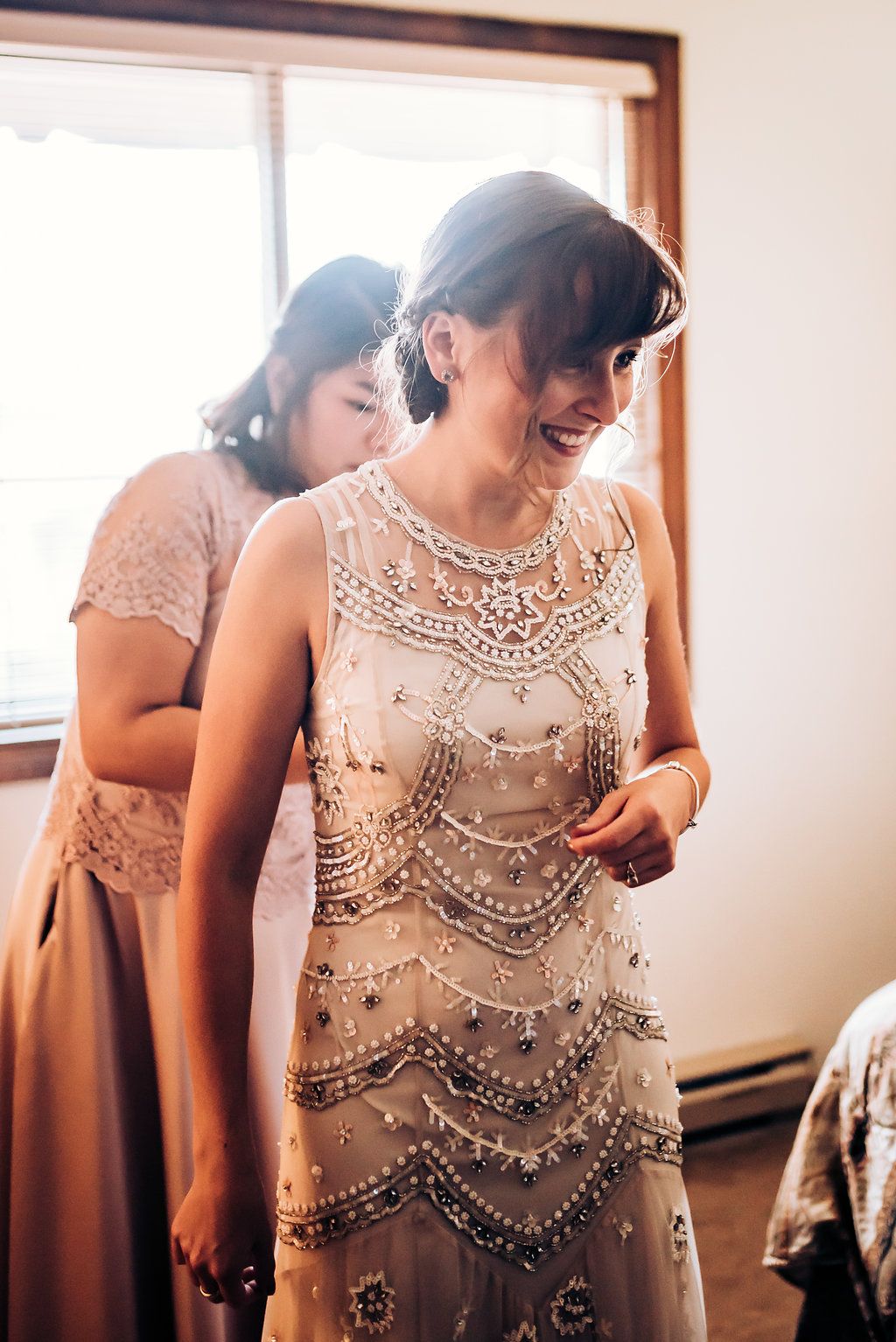 A beaded vintage-style dress sparkles in natural window light during a wedding preparation.