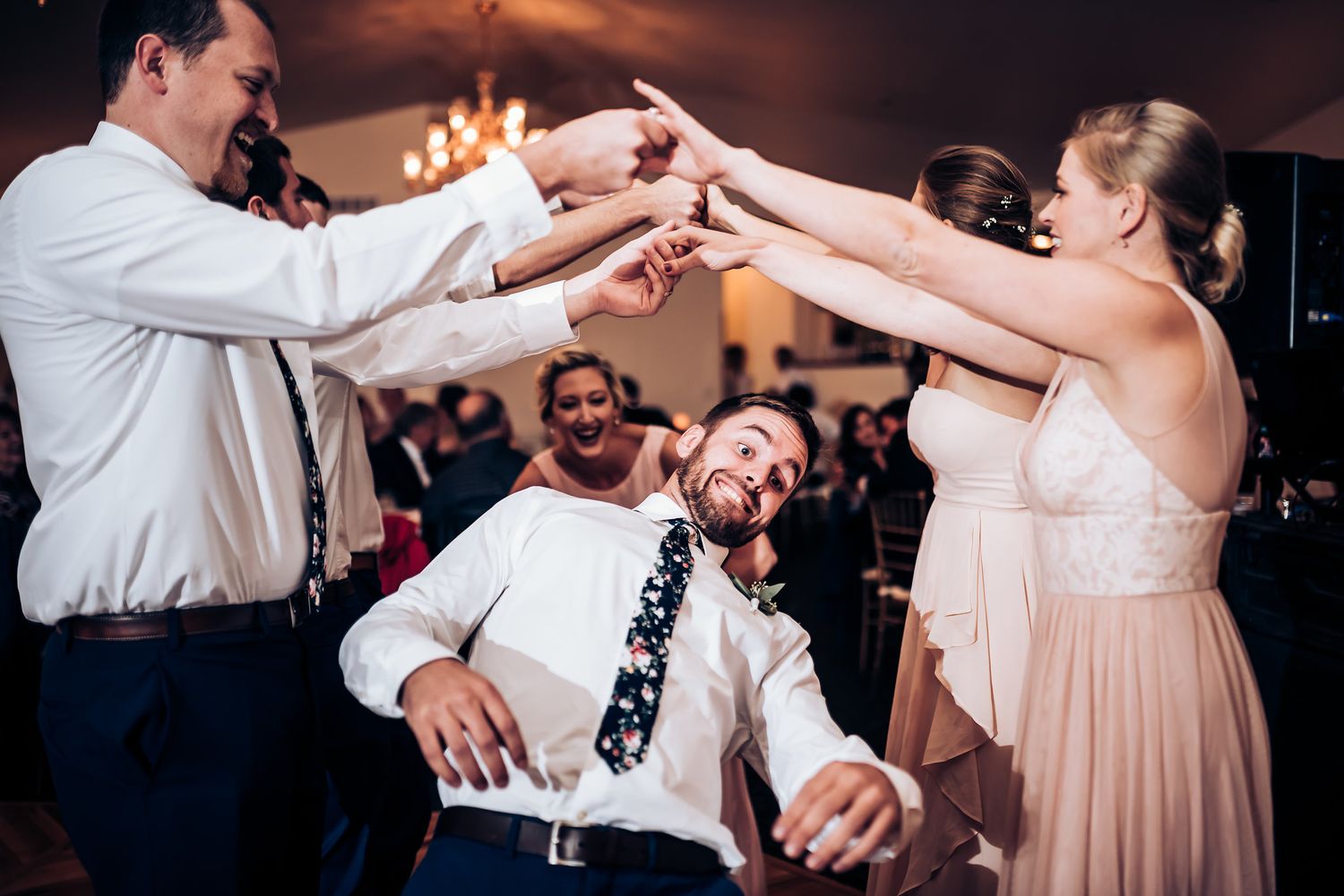Wedding party dancing in a circle creating a fun moment on the dance floor under warm lighting.