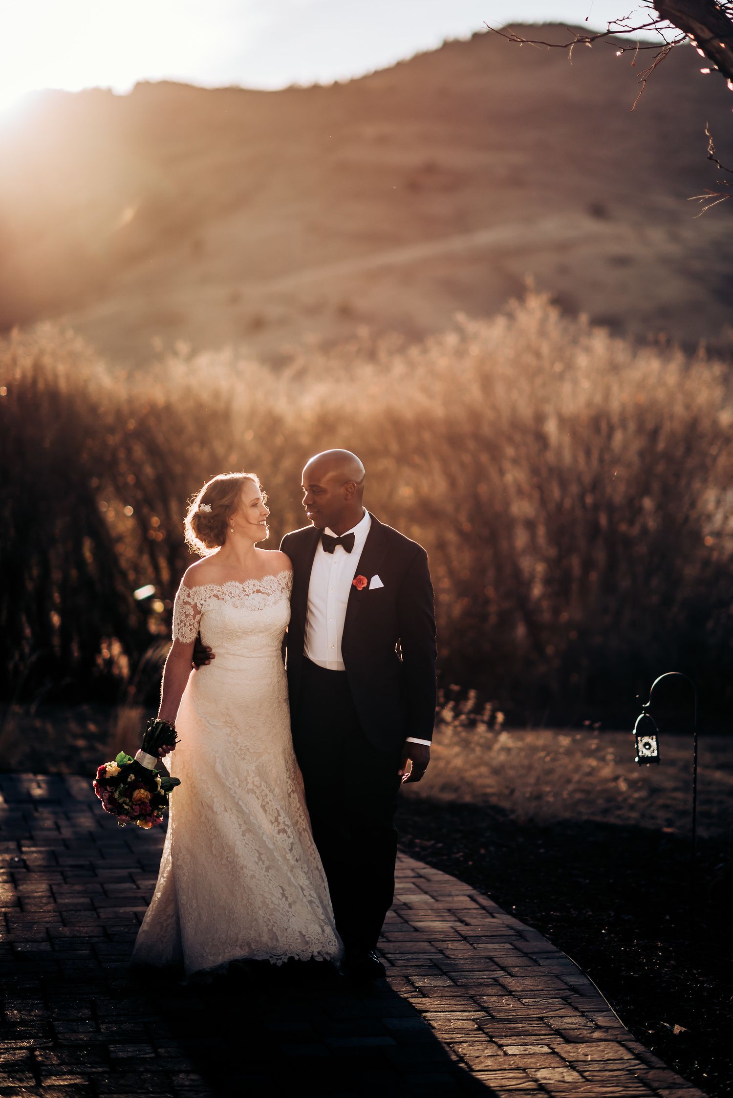 Elegant bride and groom walking together at sunset against a mountain backdrop.