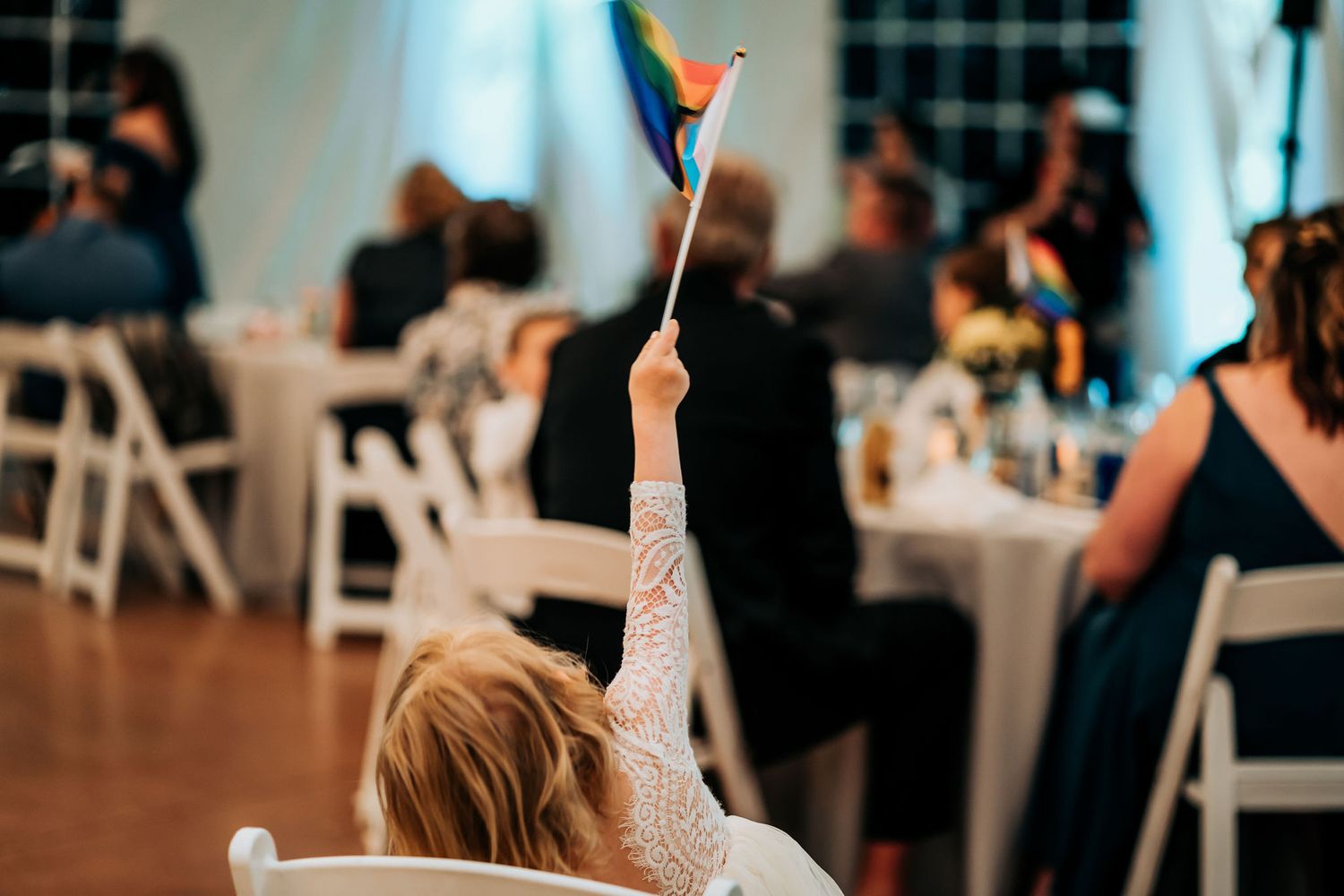Wedding guest raises party prop during reception celebration in an indoor venue with string lights.