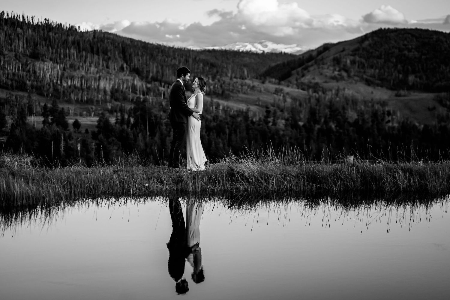 Black and white wedding photo with couple's reflection in mountain lake.