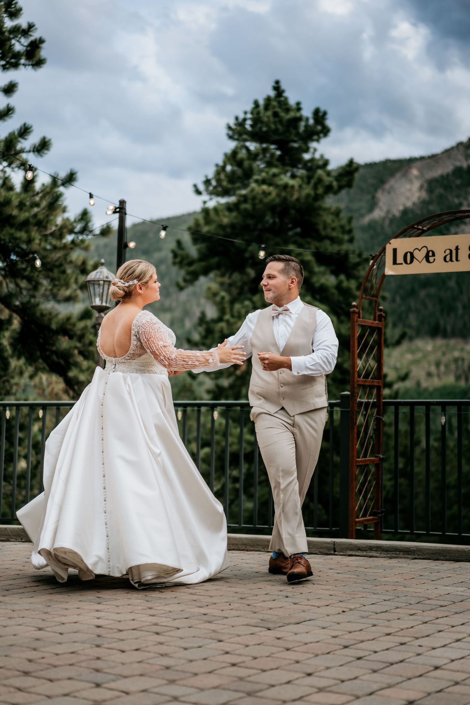 A couple dances on an outdoor terrace with mountain views during their wedding celebration.