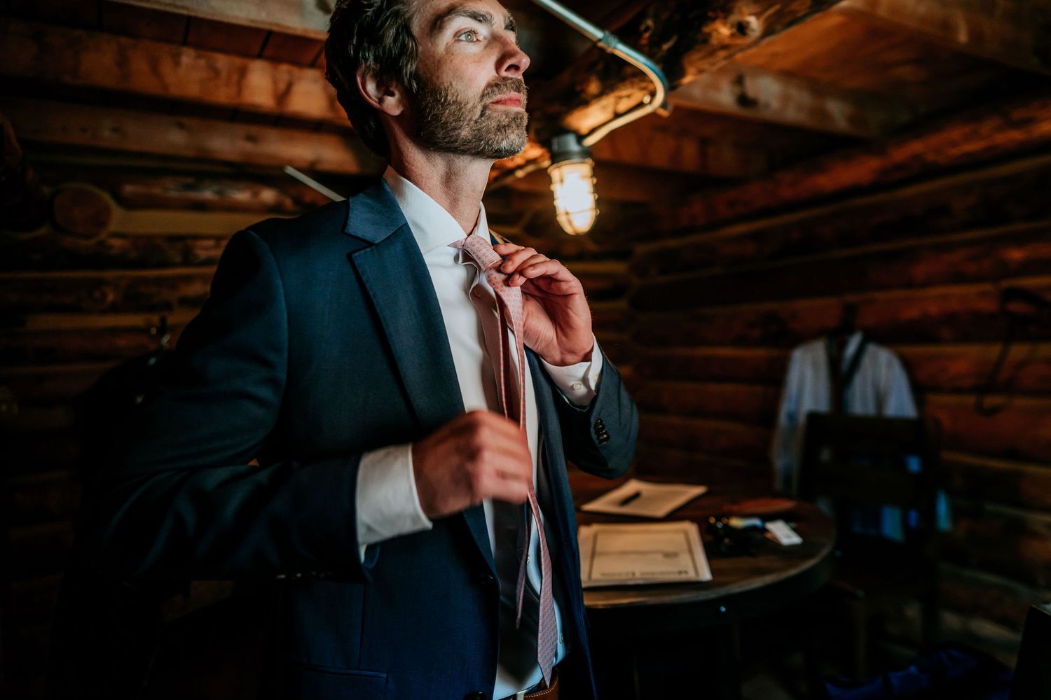 Person in formal attire adjusting tie in rustic cabin setting.