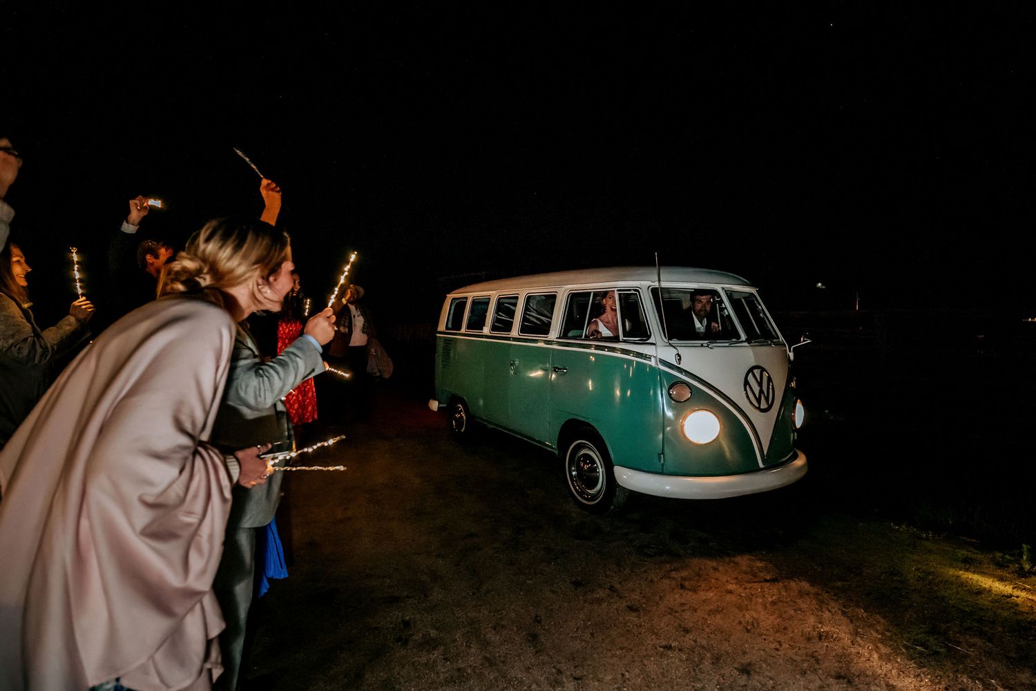 Classic mint green VW bus parked at night while wedding guests hold sparklers.