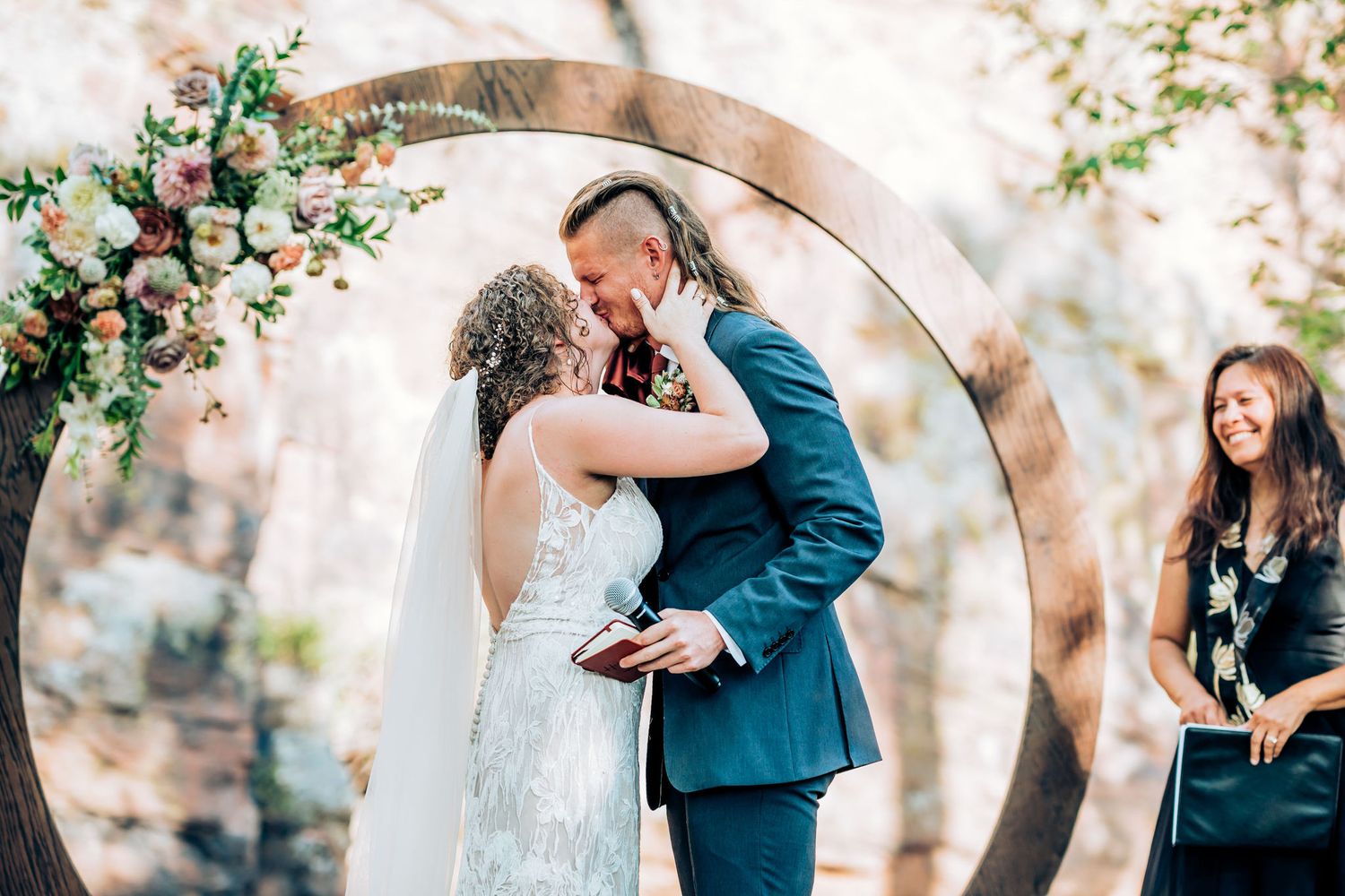 Romantic moment captured during wedding ceremony under a circular floral arch.