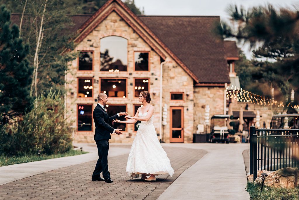 A couple dancing together outside a beautiful stone lodge decorated with string lights.