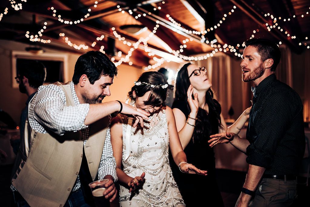 Guests dance energetically at a wedding reception under warm ambient lighting.