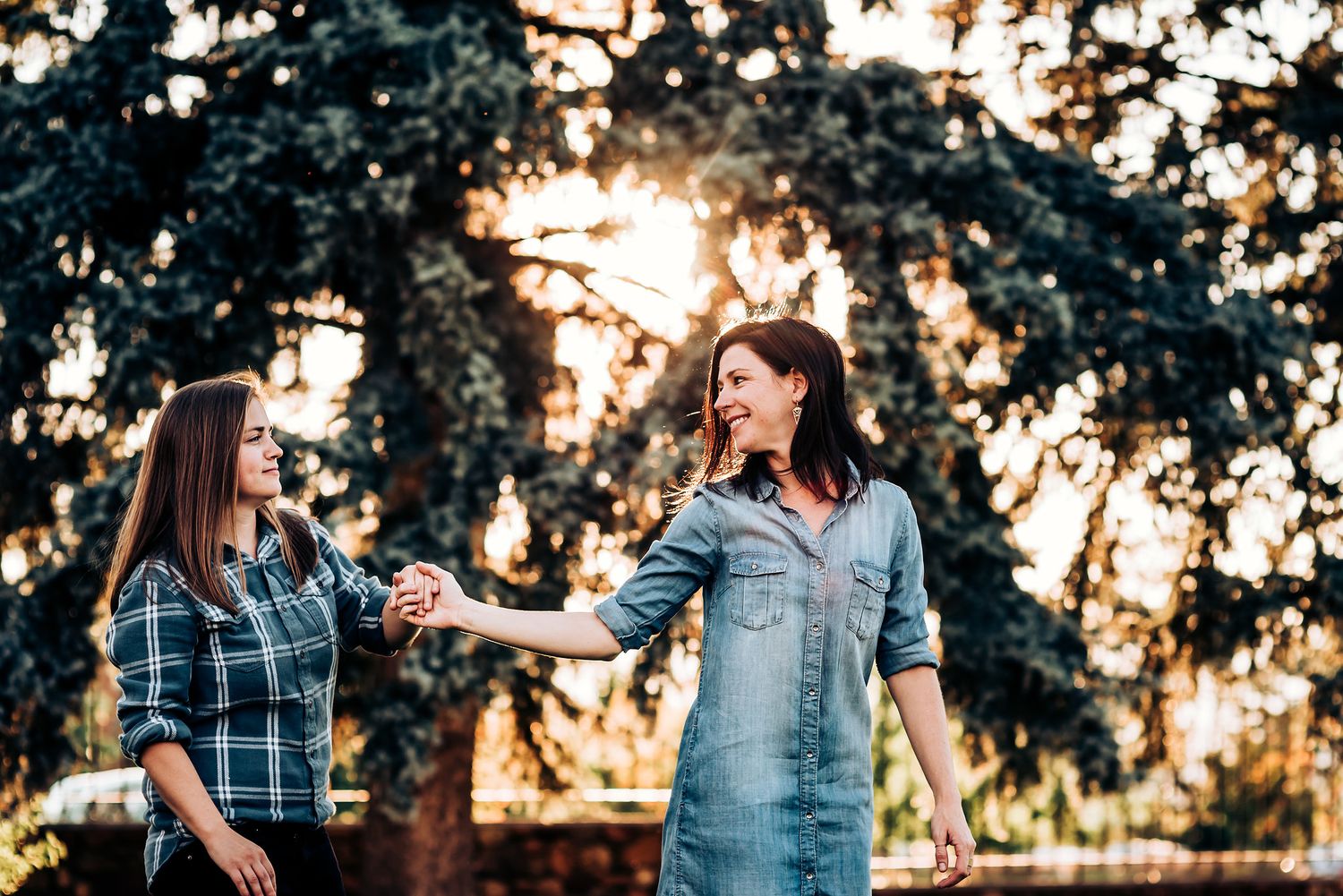 Playful interaction in denim and plaid outfits during sunset photoshoot.