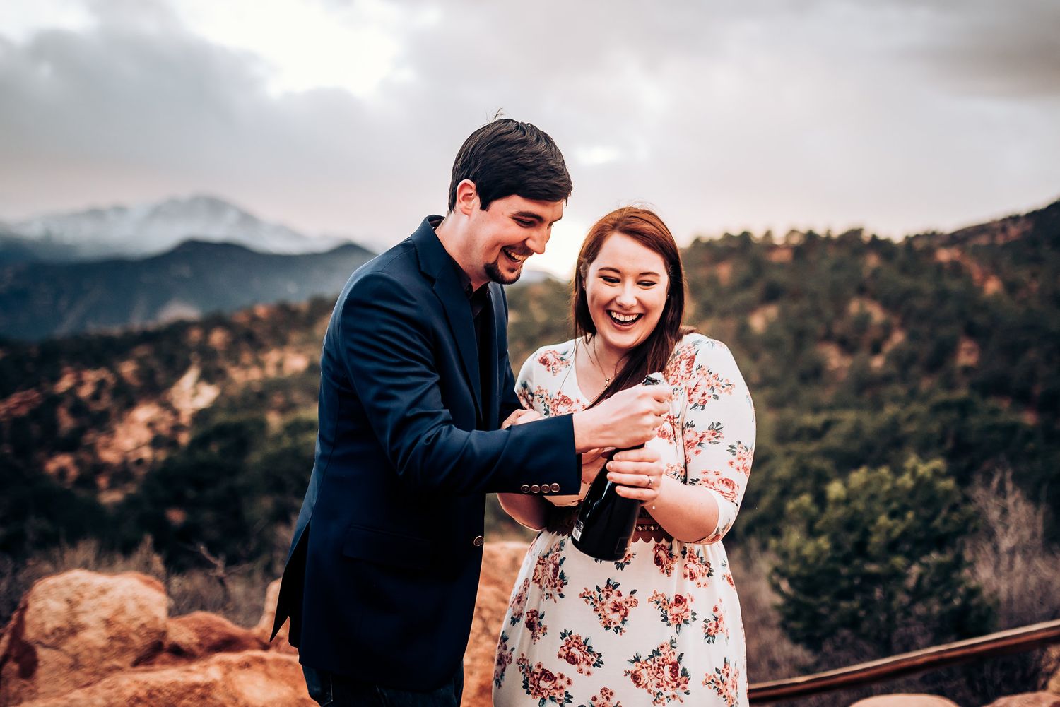 A joyful couple shares champagne while celebrating on a mountain vista.