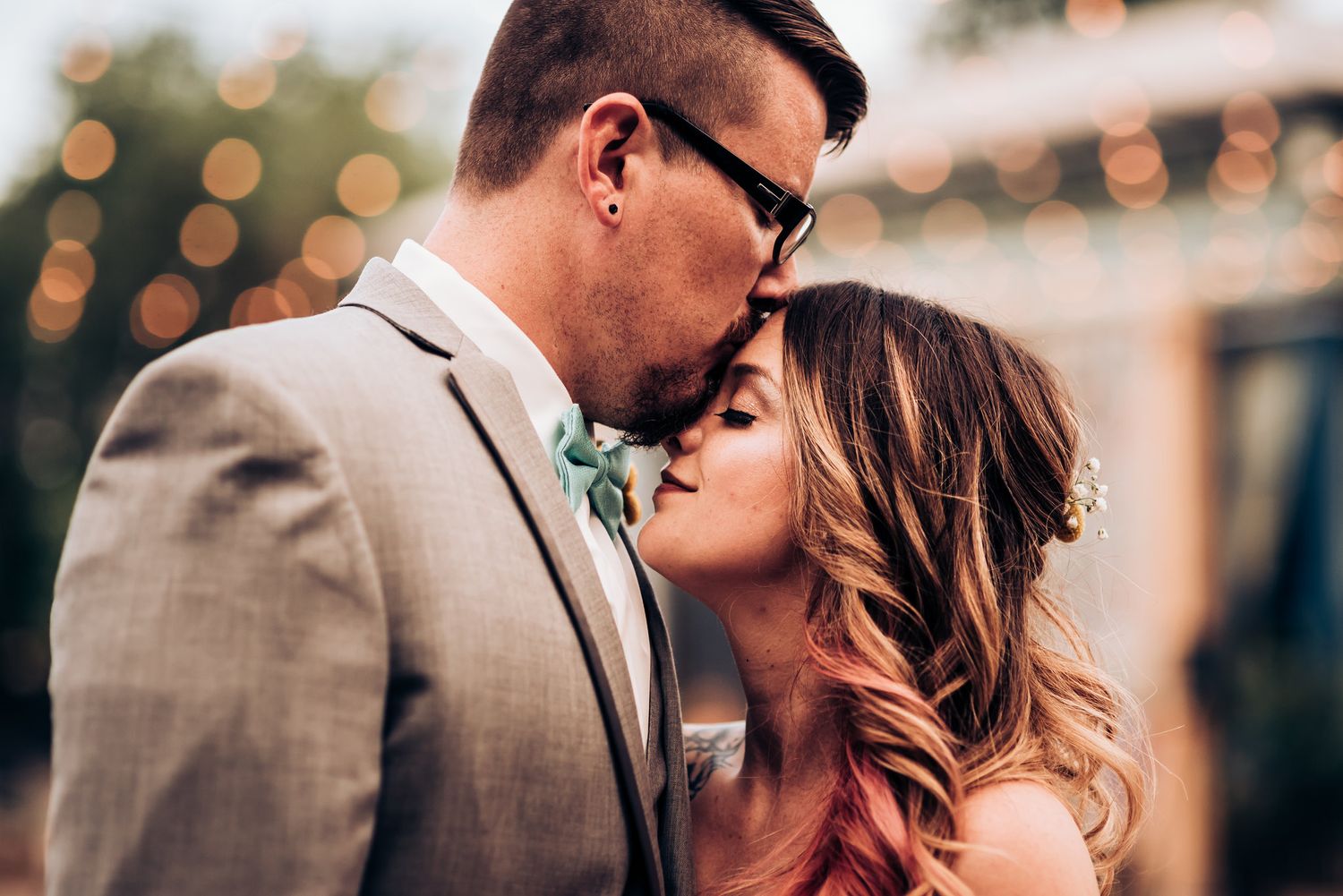 An intimate wedding portrait with soft bokeh lights and greenery in the background.