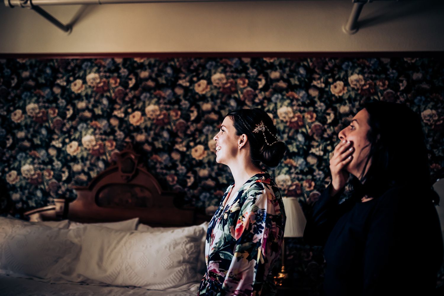 Two joyous individuals share a side-splitting laugh in front of a floral backdrop during pre-wedding festivities.