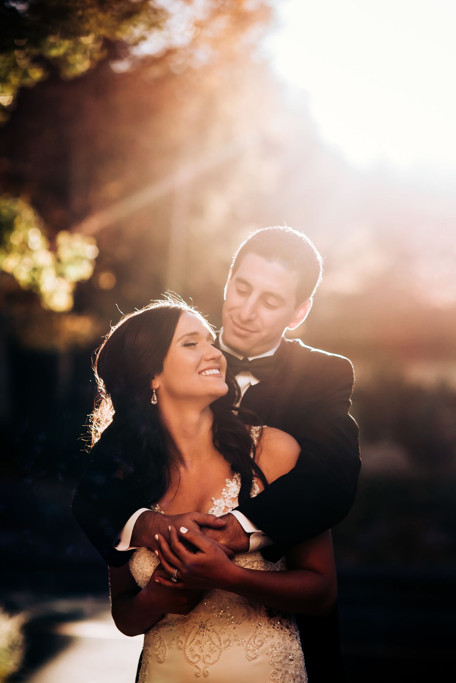 A romantic golden hour embrace between newlyweds with sunlight creating a warm backlit glow.