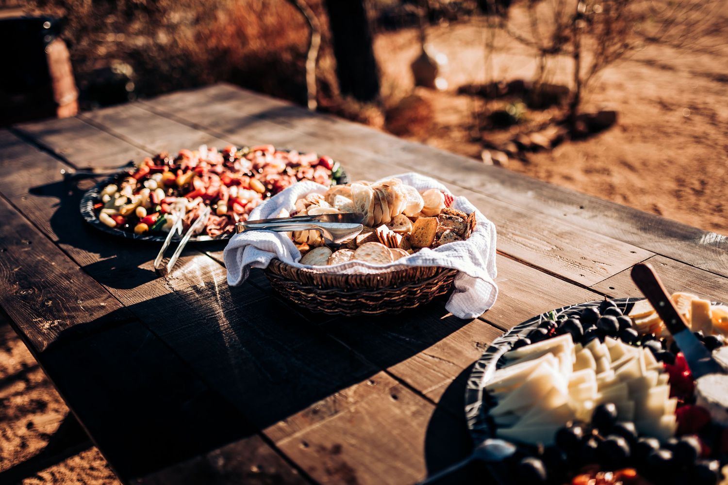 Appetizer platters with assorted meats and cheeses displayed on wooden table in desert setting.