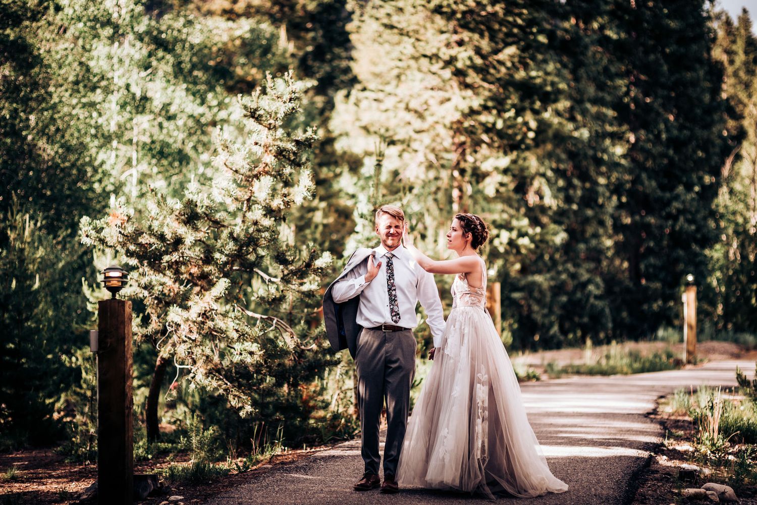 Newlyweds walking together and celebrating on a tree-lined path in formal wedding attire.