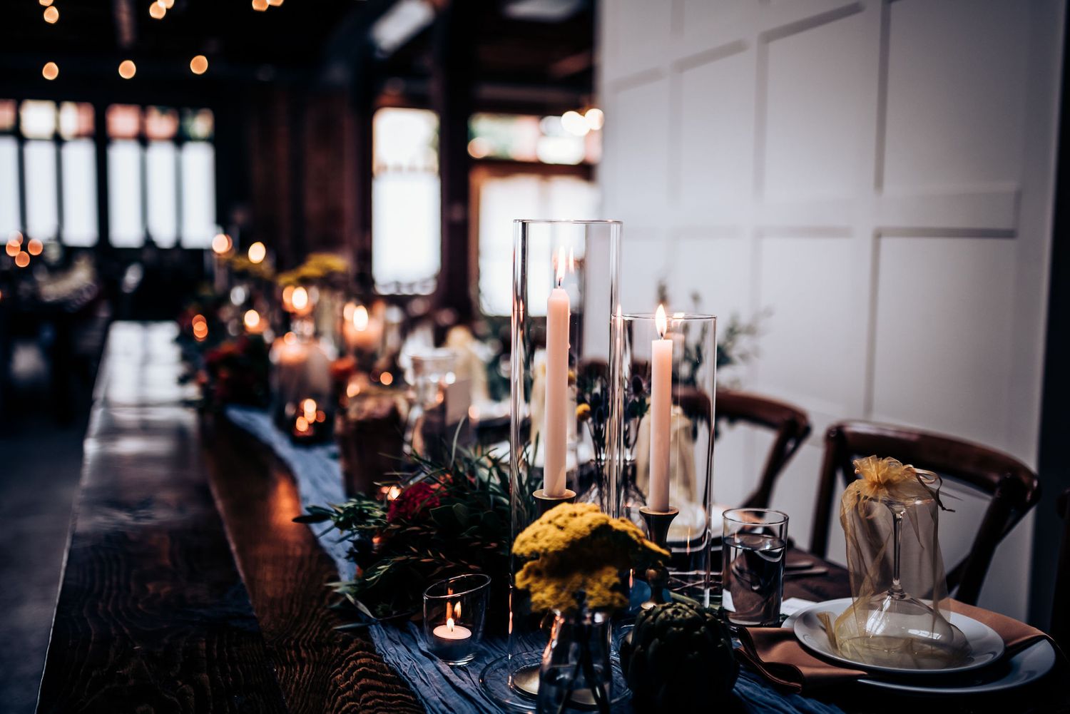 Elegant table setting with tall candles and floral decor in moody reception lighting.