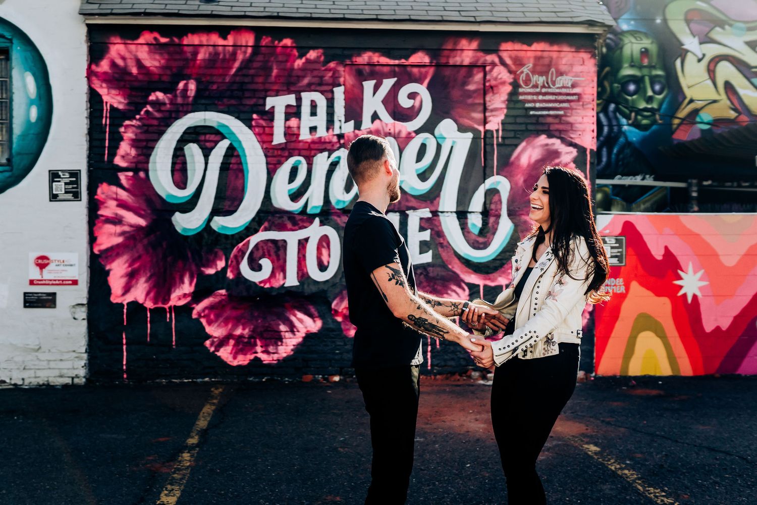Couple holds hands while standing in front of colorful urban street art wall.